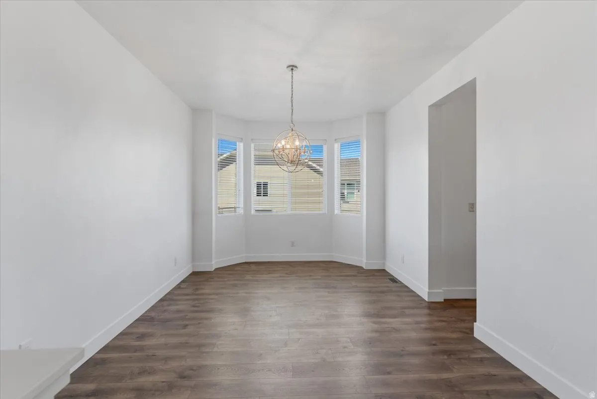 Spacious room featuring a bay window, wood-finish flooring, white baseboards, a contemporary spherical chandelier, and an open doorway