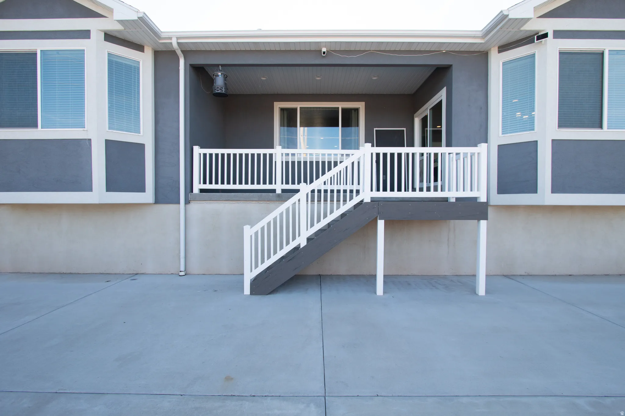 Rear exterior with a concrete patio, covered patio space, white railing, and exterior staircase