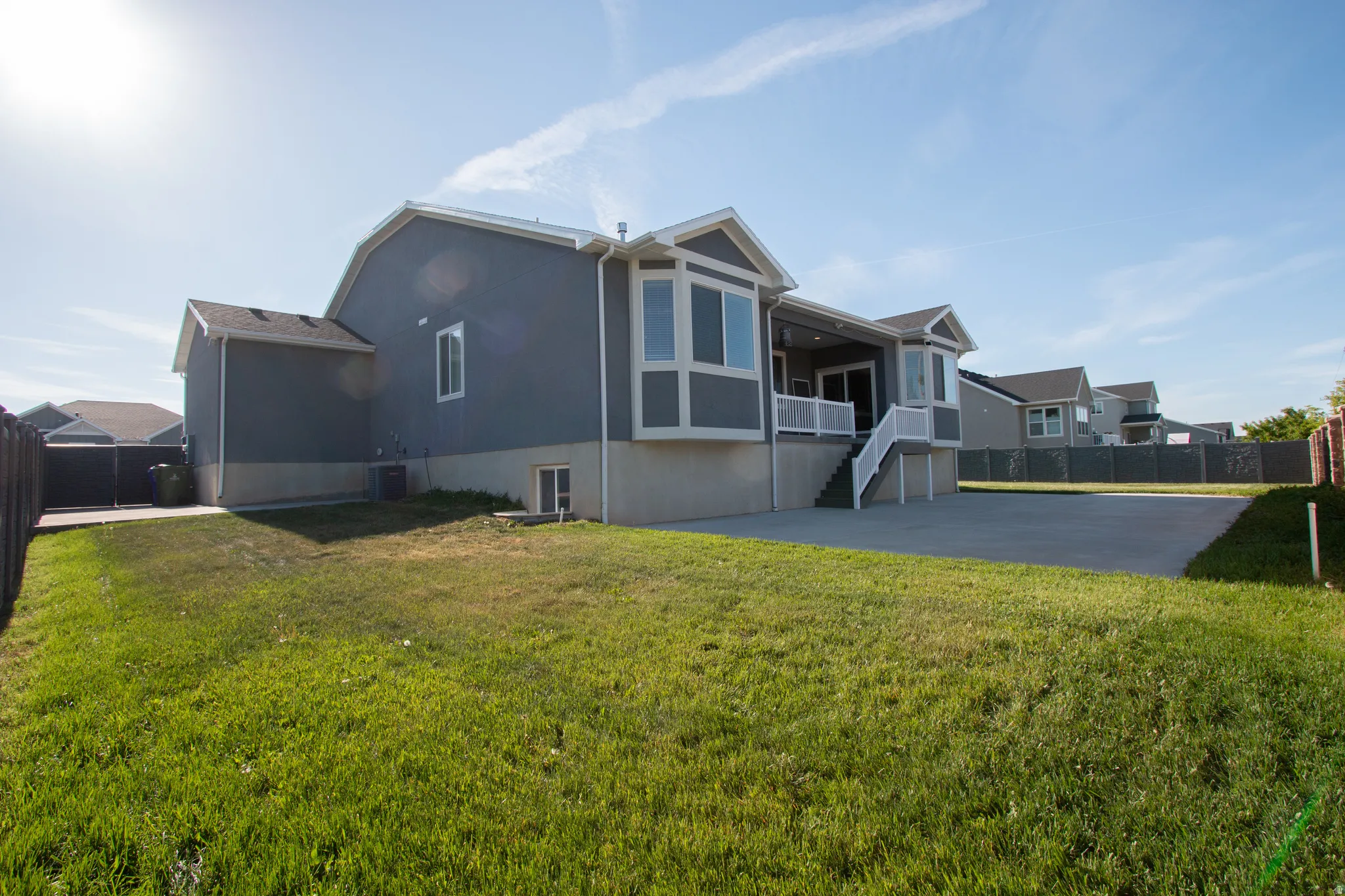 Expansive backyard featuring a large concrete patio, manicured lawn, and a multi-level house with a deck and bay windows