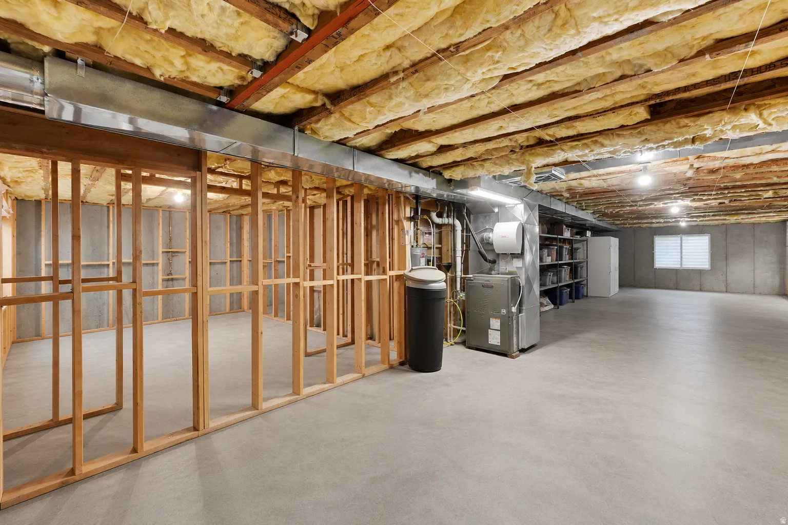 Unfinished basement with concrete flooring, exposed wood ceiling joists, and visible insulation