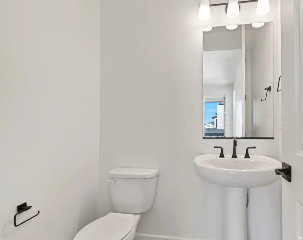 Pedestal sink with a matte black faucet, wall-mounted mirror, and vanity lighting