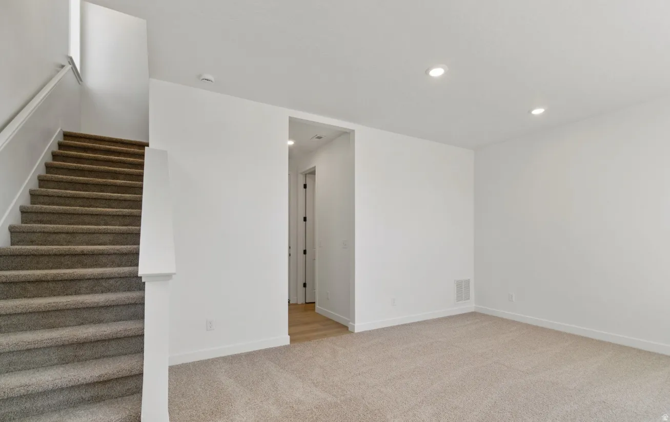 Neutral tone carpet flooring and crisp white walls characterize this interior space, featuring a staircase with matching carpet treads and a white handrail
