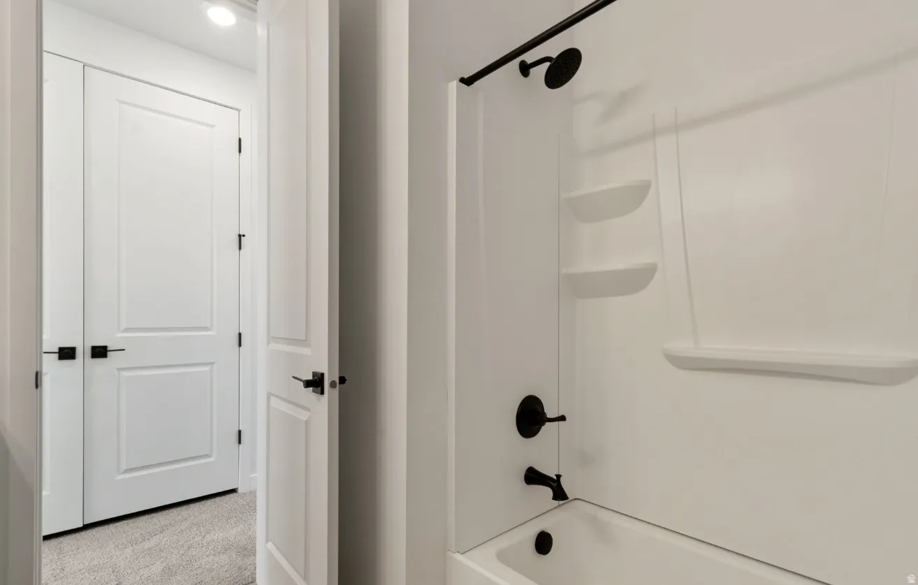 White tub shower combination featuring black matte fixtures, integrated shelving, and a clean white surround