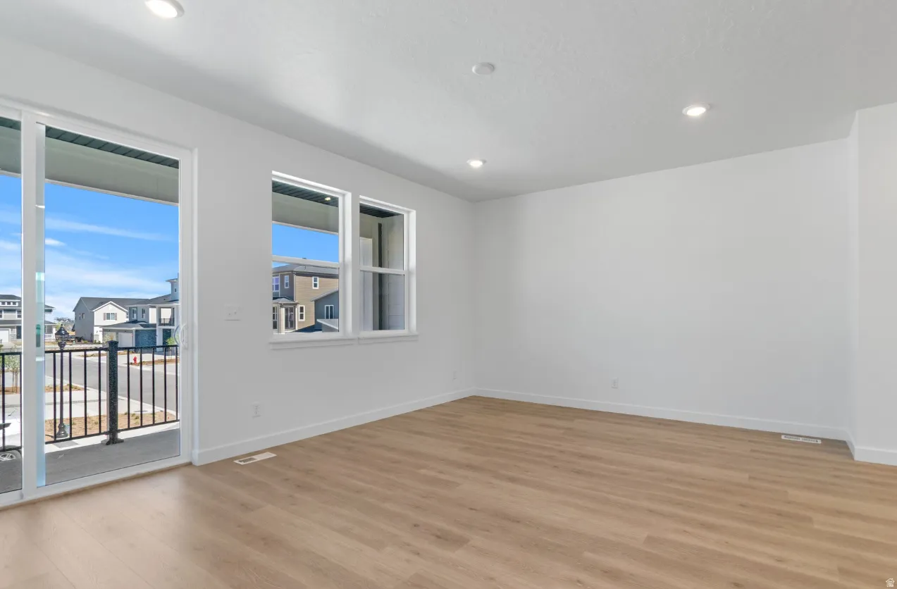 Bright interior featuring wood-finish flooring, recessed lighting, white walls, multiple windows, and a sliding glass door opening to a balcony with black railings