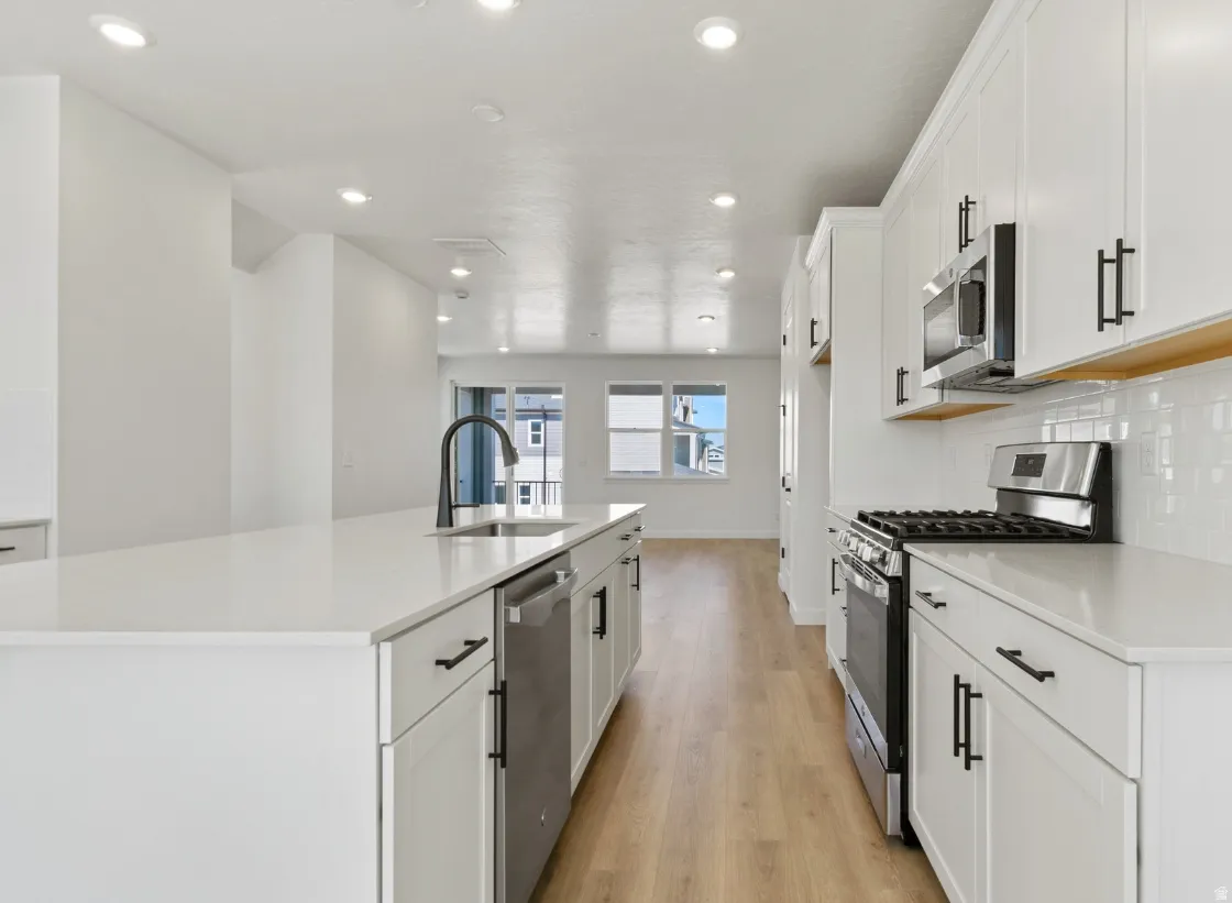 Contemporary kitchen featuring an expansive island with a matte black faucet, stainless steel appliances, white subway tile backsplash, and light wood-finish flooring