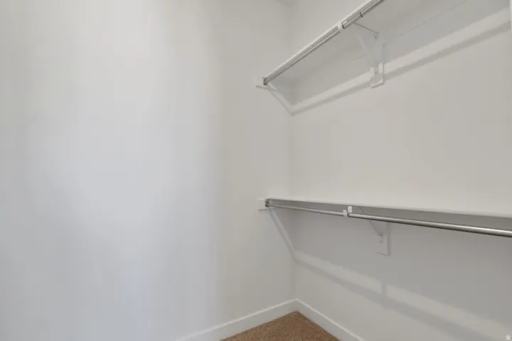 Walk-in closet featuring white walls, white shelving, and chrome hanging rods