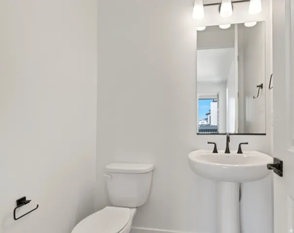 Pedestal sink with a matte black faucet, wall-mounted mirror, and vanity lighting