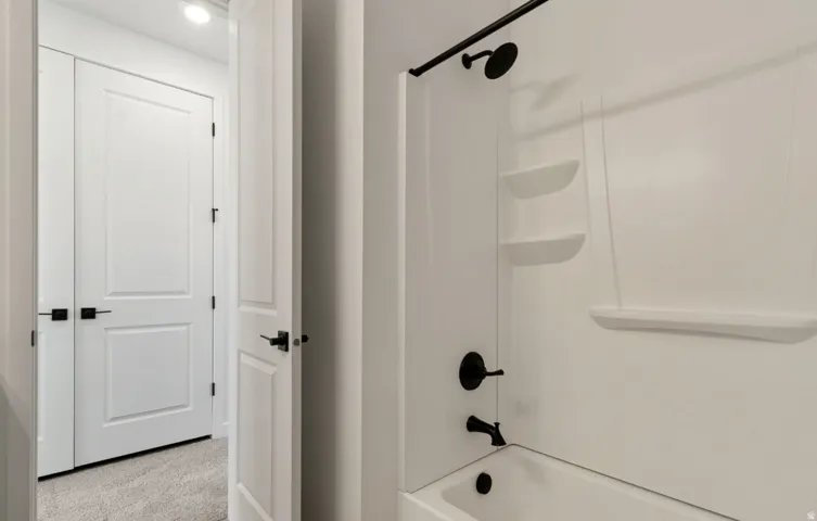 White tub shower combination featuring black matte fixtures, integrated shelving, and a clean white surround