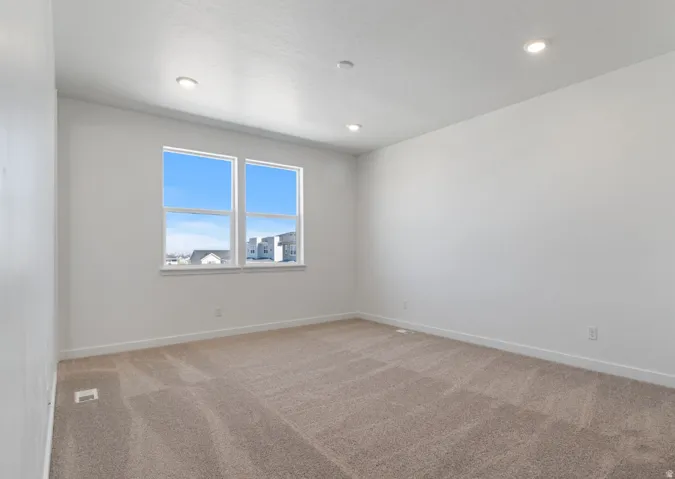 Spacious room featuring neutral carpeting, recessed ceiling lighting, and two large windows with white trim