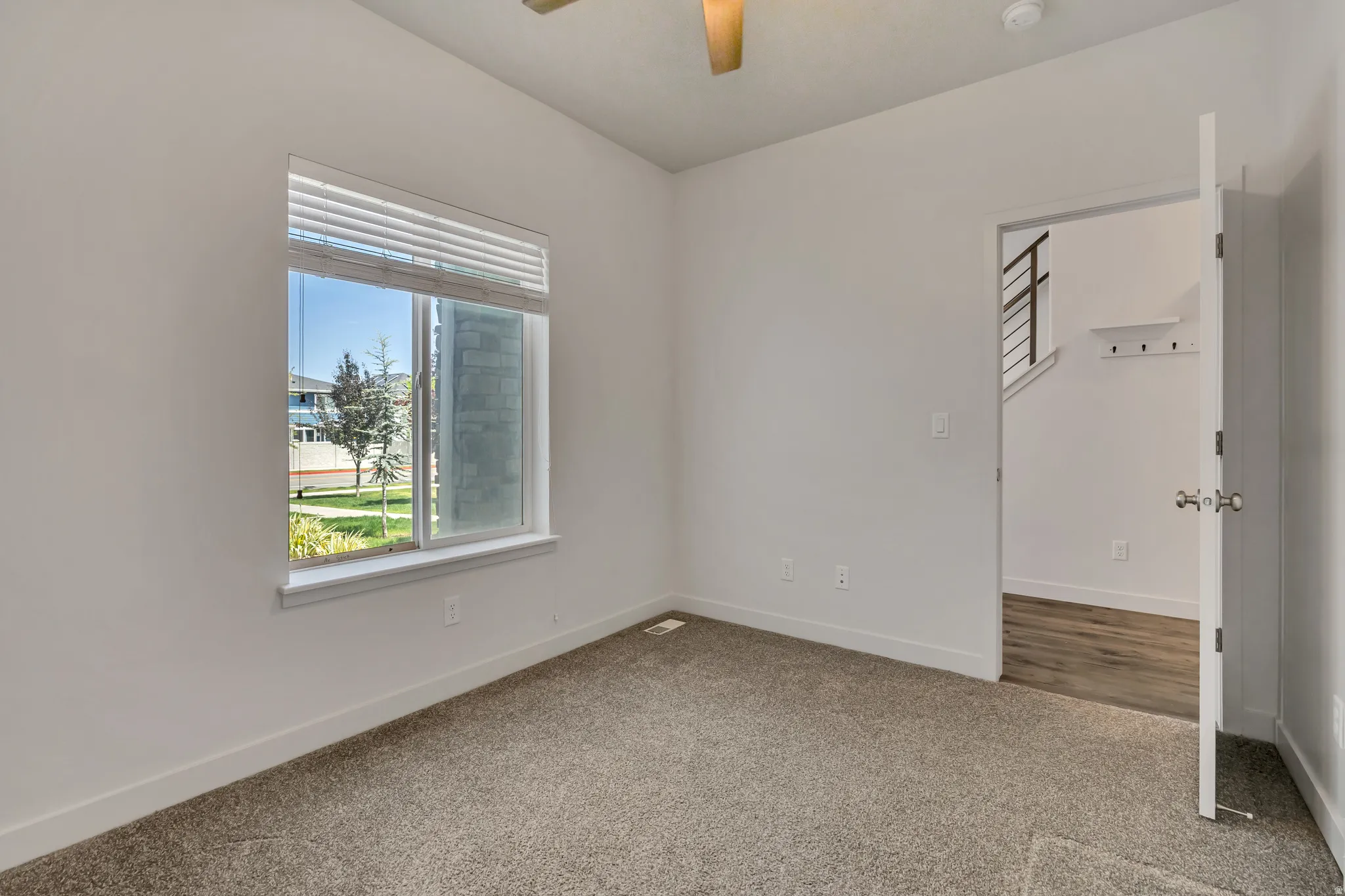 Bright room with neutral carpeting, white walls, and a large window with horizontal blinds