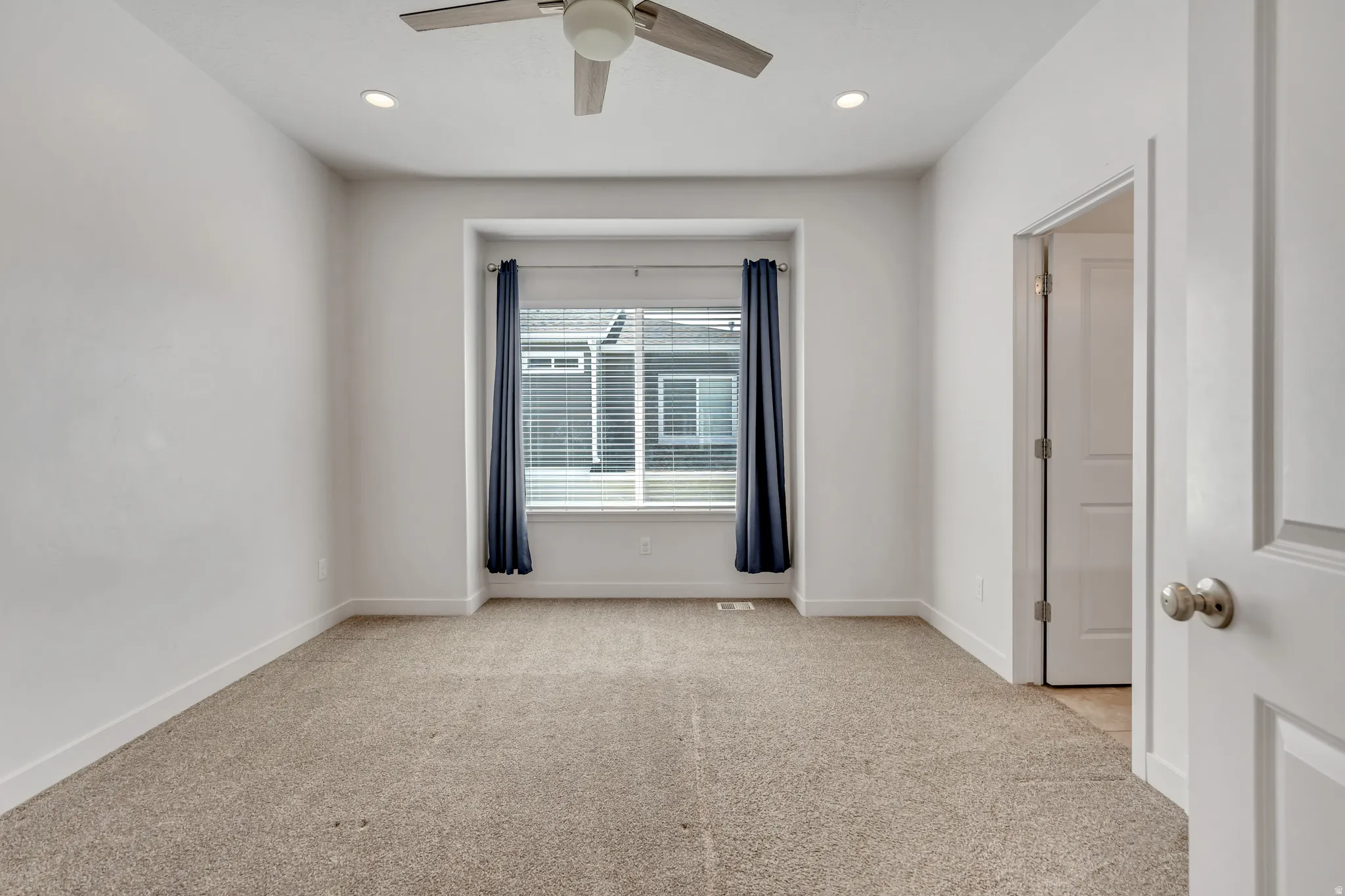 Carpeted interior space featuring a recessed window, a ceiling fan with integrated lighting, and recessed ceiling lights