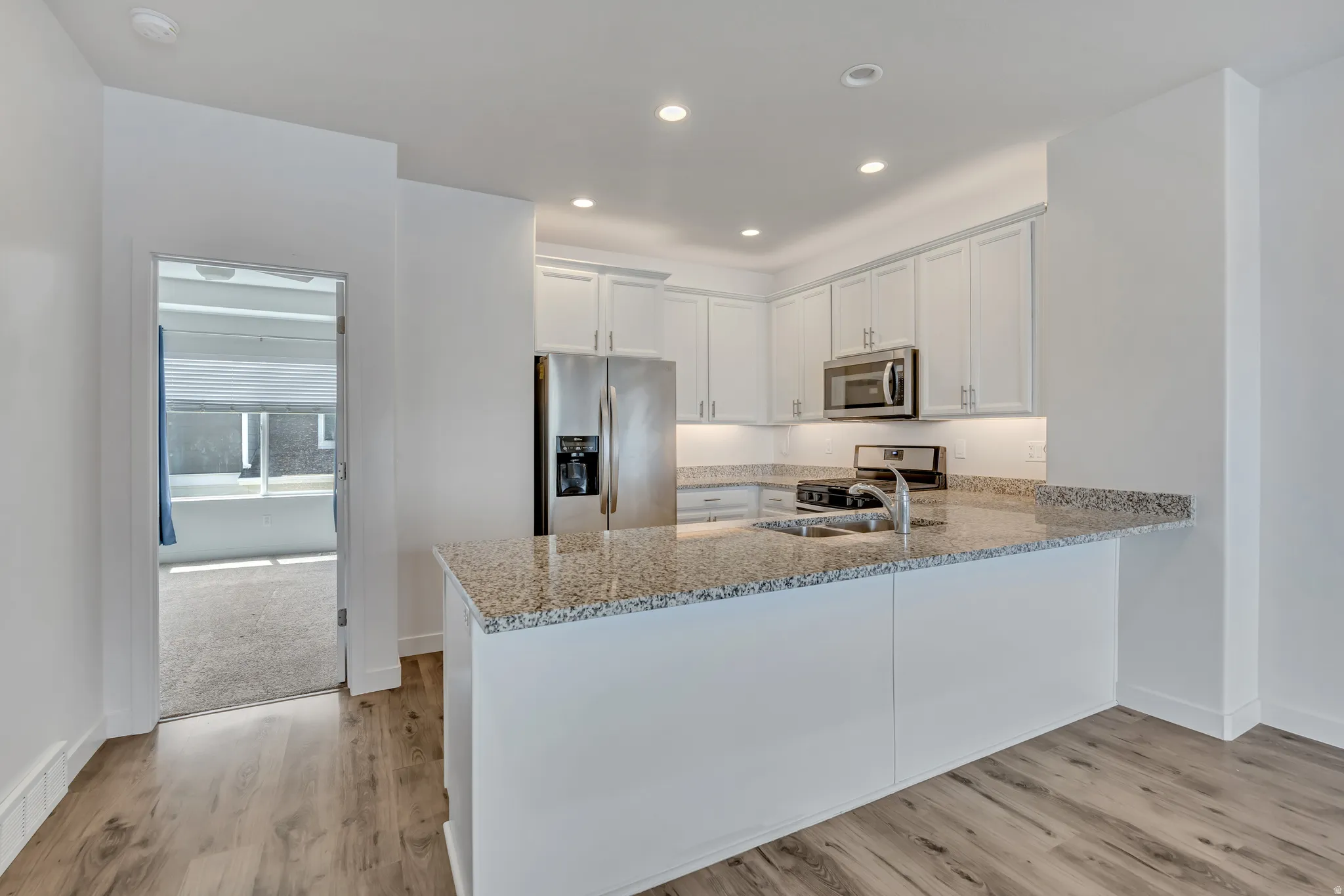 Modern kitchen featuring granite countertops, white cabinetry, stainless steel appliances, wood-finish flooring, and recessed lighting
