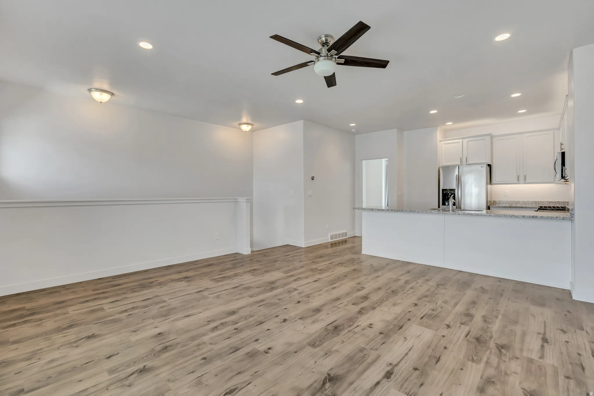 Open-concept living space featuring wood-finish flooring, a ceiling fan with integrated lighting, and recessed lighting