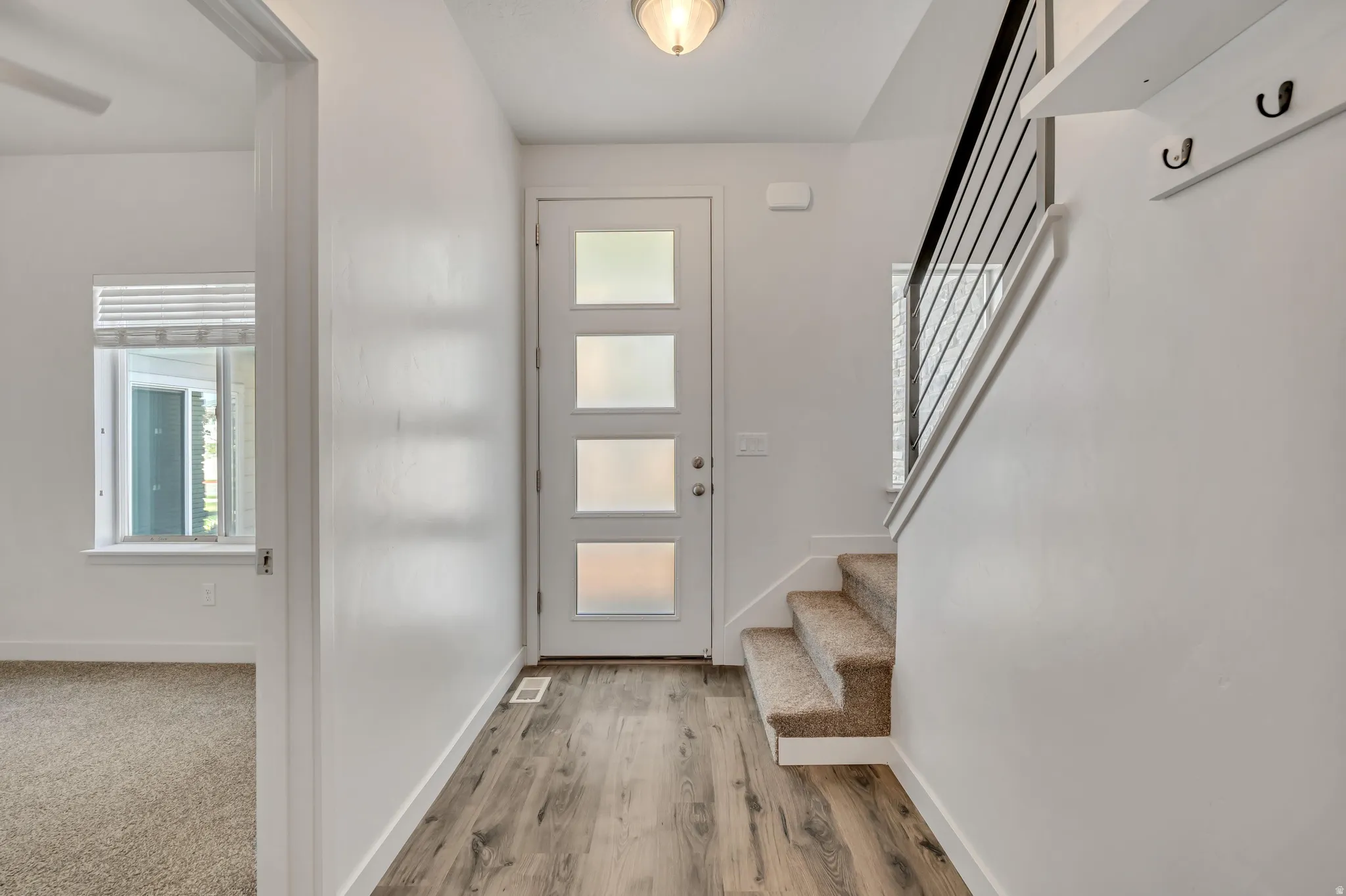 Entryway featuring a modern front door with frosted glass panels, wood-finish flooring, and a carpeted staircase with a black metal railing