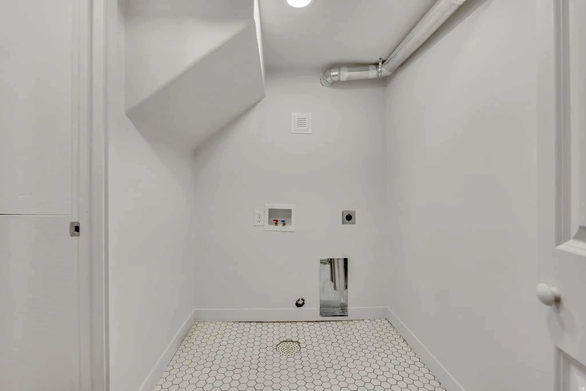 Dedicated utility area featuring white hexagonal floor tiles and modern white walls