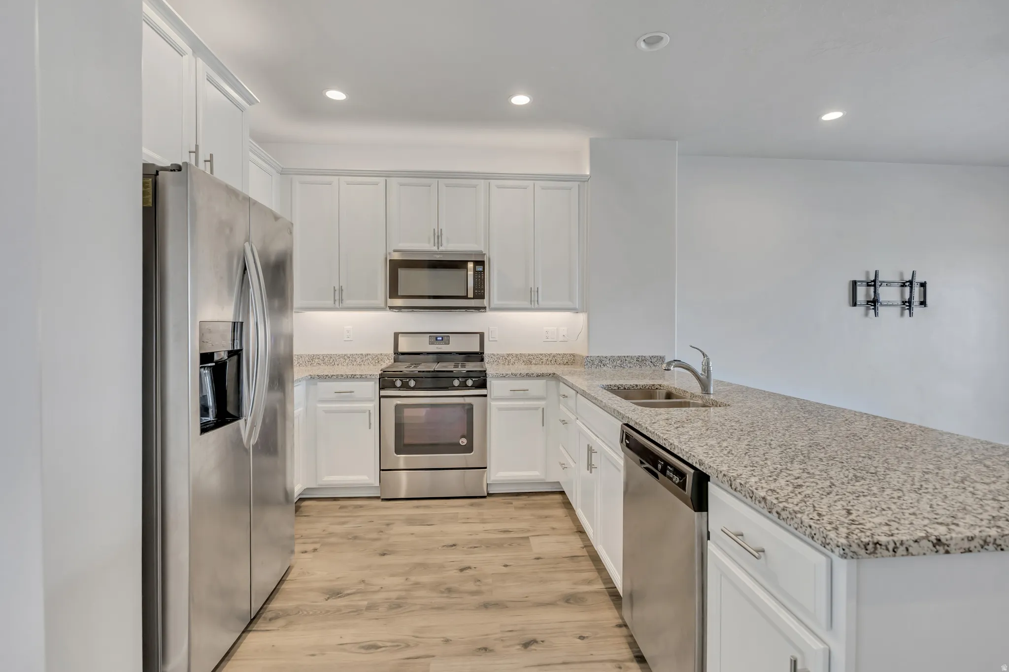 Modern kitchen featuring white cabinetry, stainless steel appliances, light granite countertops, a stainless steel sink with a gooseneck faucet, and wood-finish flooring