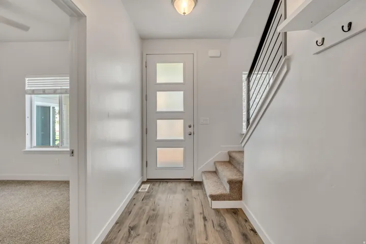 Entryway featuring a modern front door with frosted glass panels, wood-finish flooring, and a carpeted staircase with a black metal railing