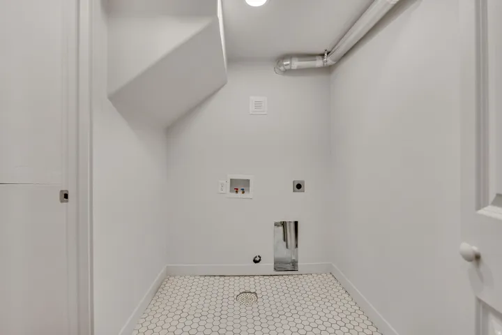 Dedicated utility area featuring white hexagonal floor tiles and modern white walls