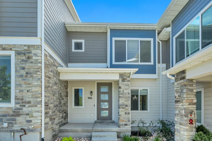 Contemporary facade featuring a prominent stone veneer accent, multi-textured siding, a covered entryway with stone-clad columns, and a modern front door with frosted glass panels