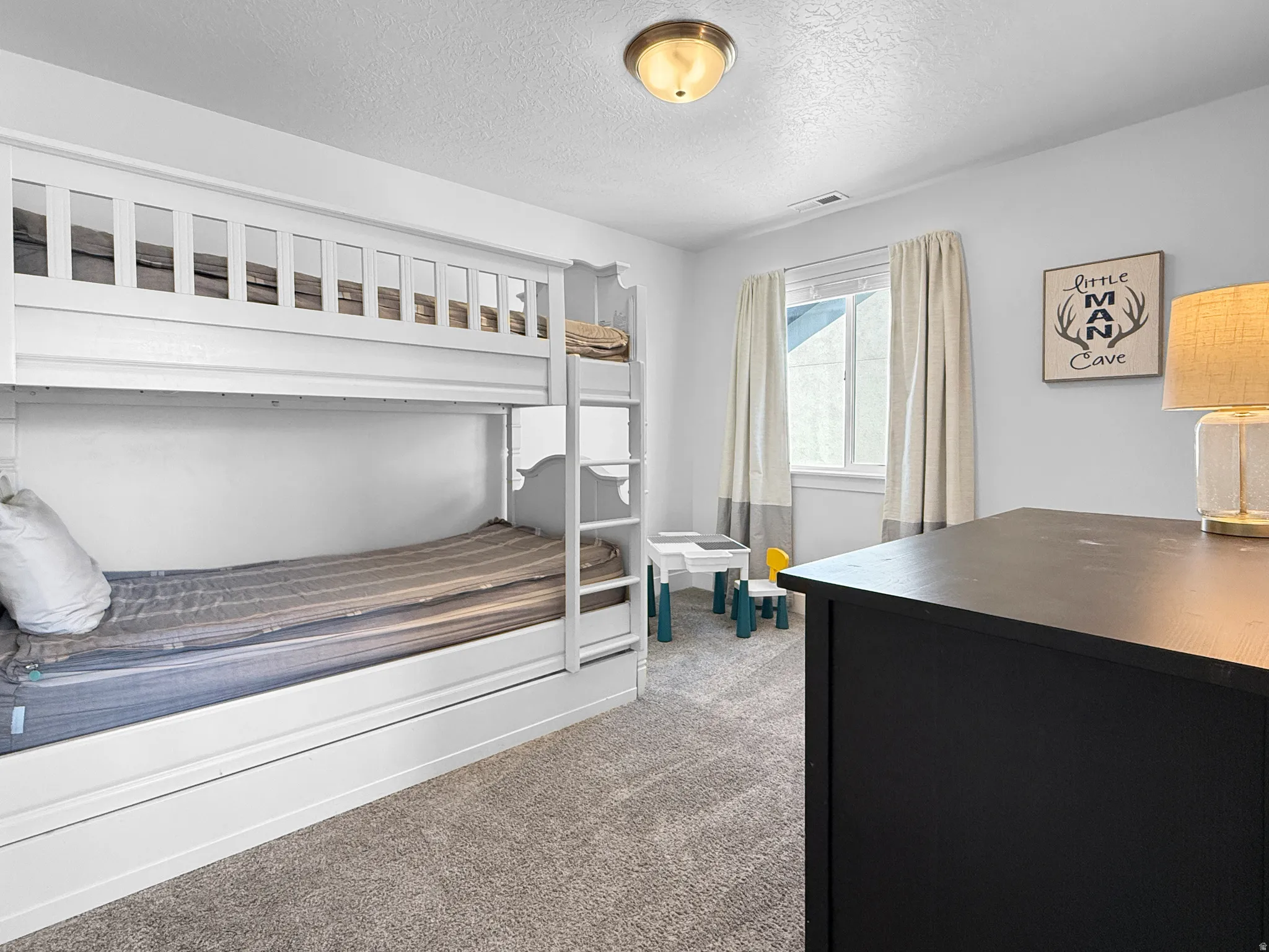 Light-filled room featuring white walls, a white bunk bed, carpeted flooring, and a flush mount ceiling light fixture