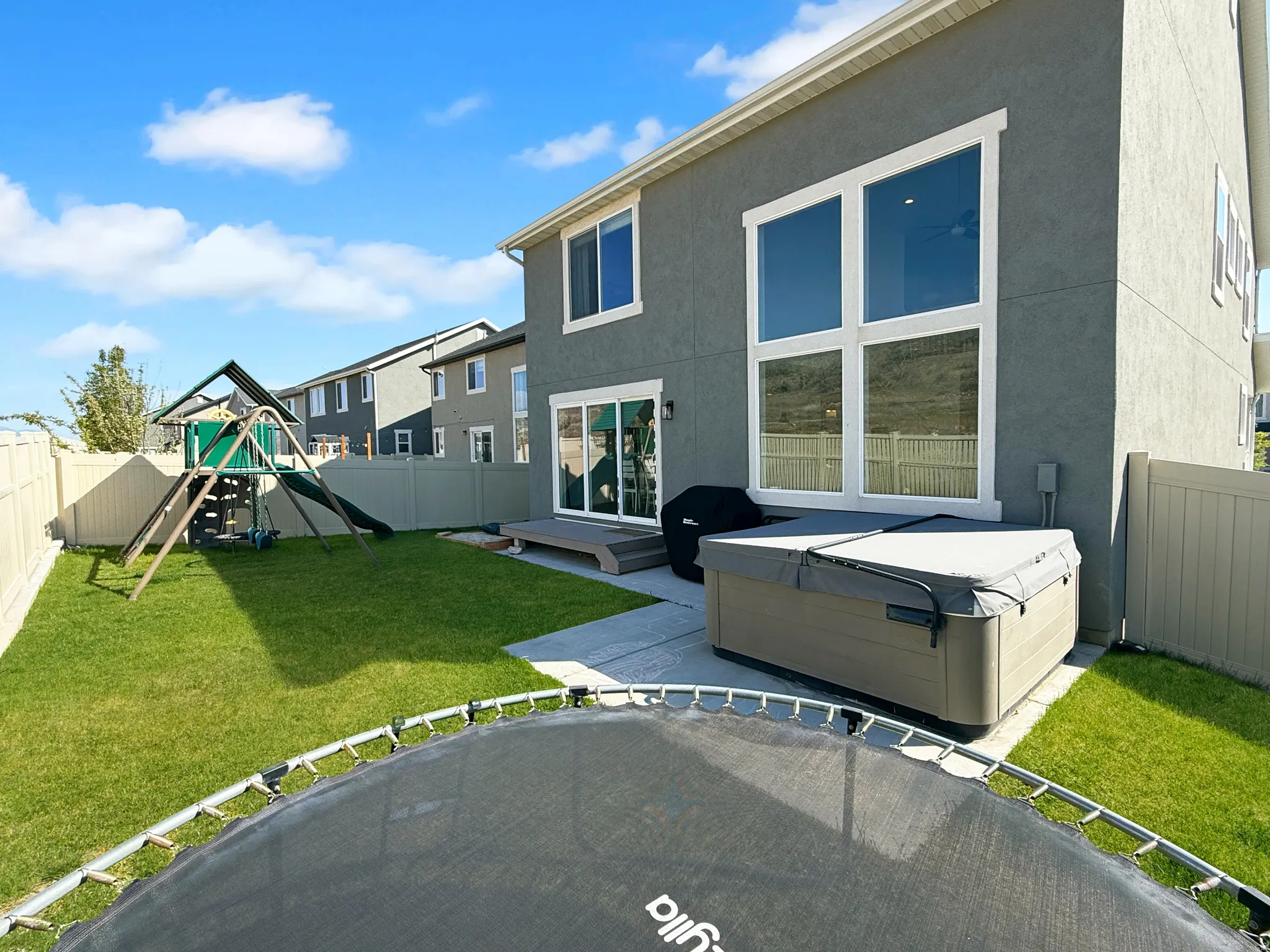 Fenced backyard with a concrete patio, green lawn, and a built-in hot tub