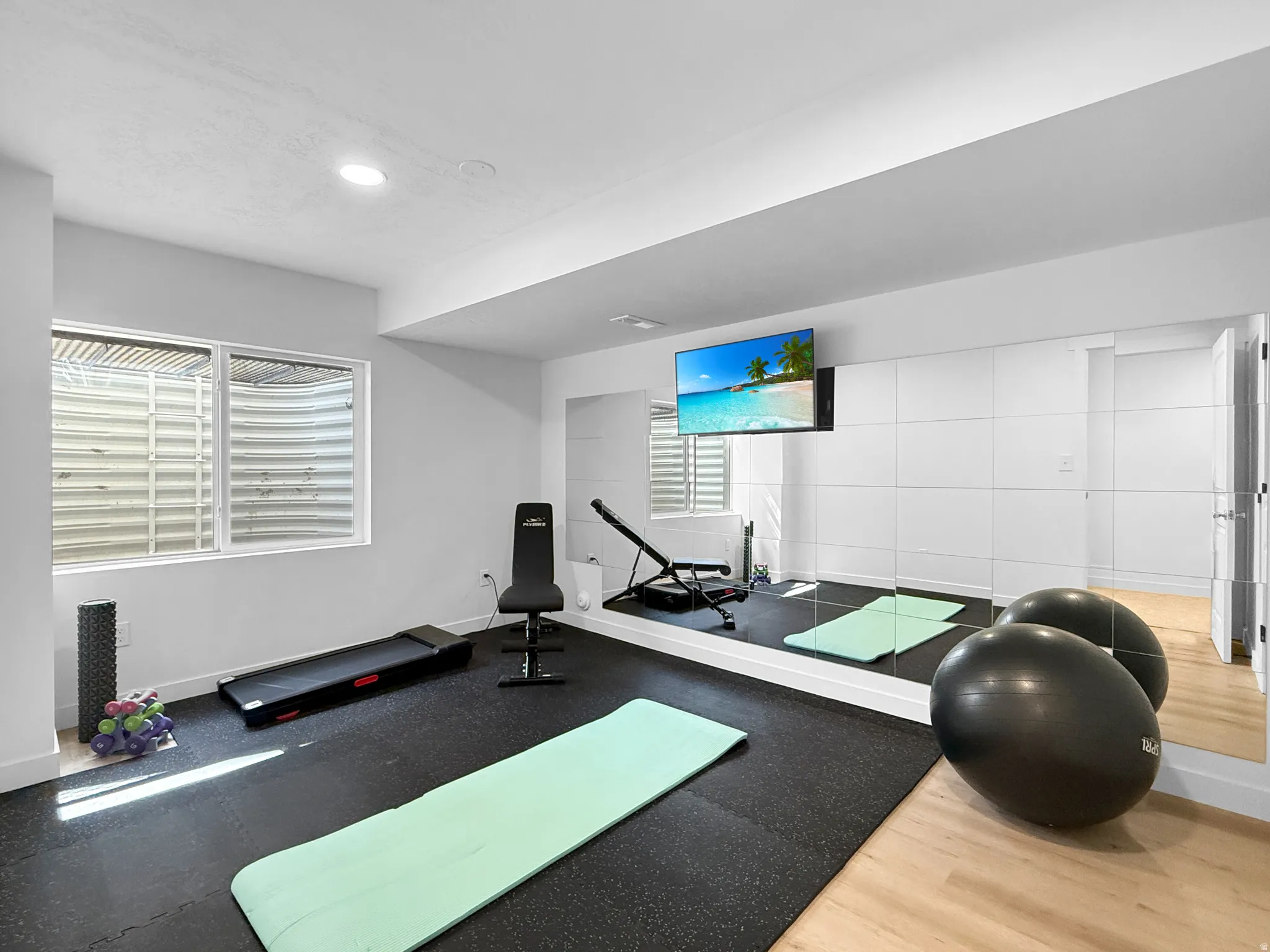Dedicated fitness area featuring wall-mounted television, full-wall mirrors, recessed lighting, and a window with blinds