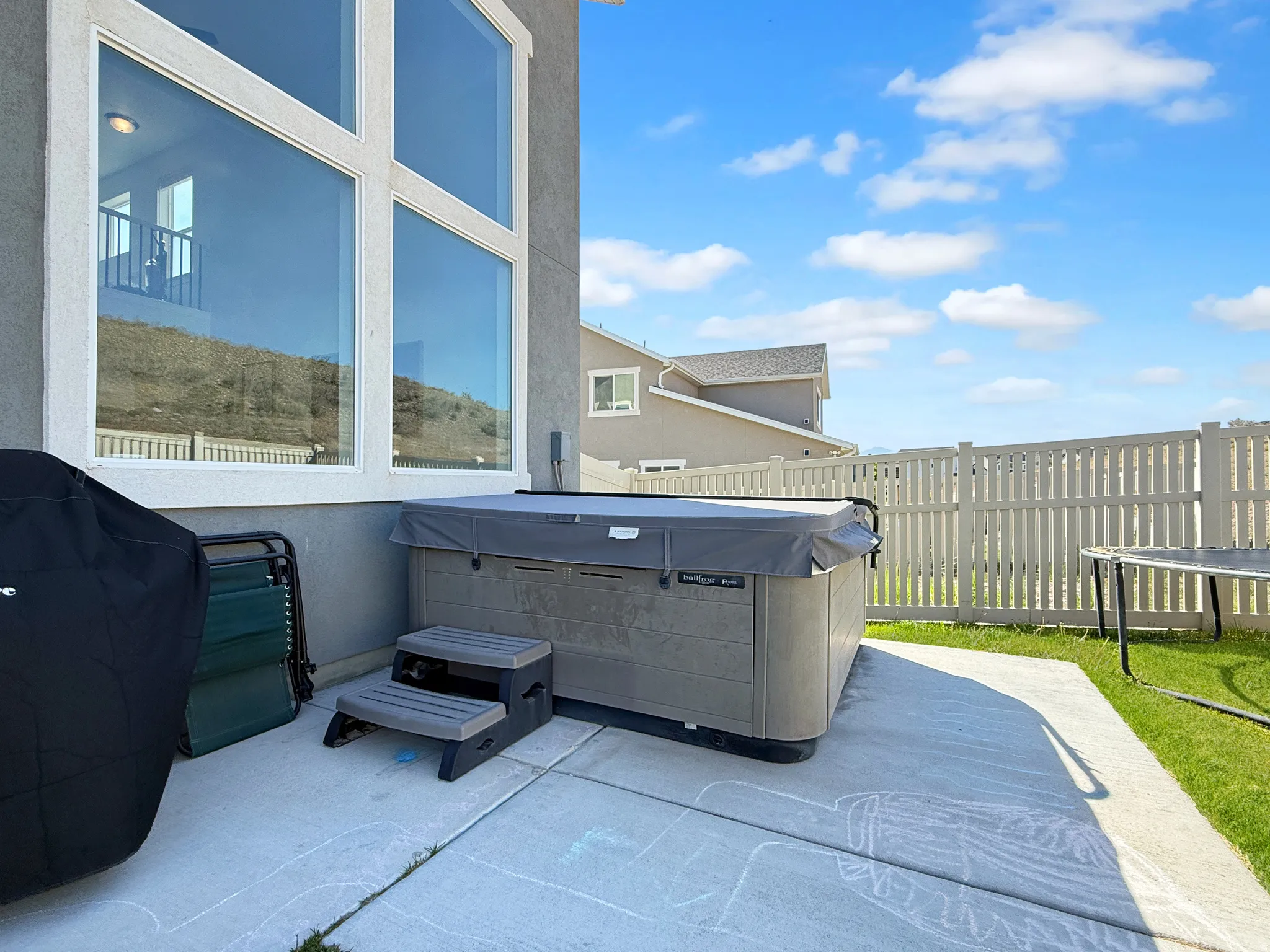 Rear patio featuring a hot tub, concrete pad, and a white picket fence enclosing the backyard