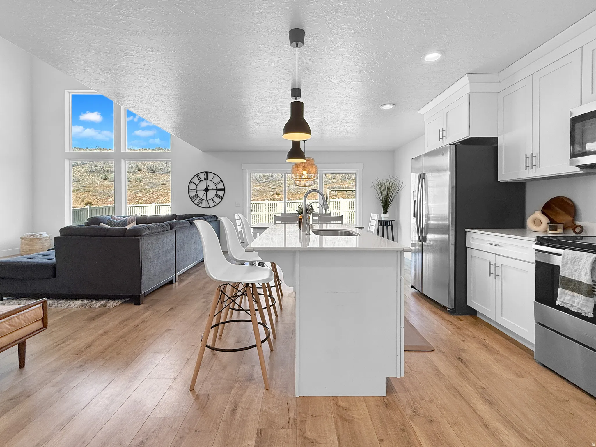 Open-concept living space featuring wood-finish flooring, a kitchen island with seating, white cabinetry, stainless steel appliances, and large picture windows