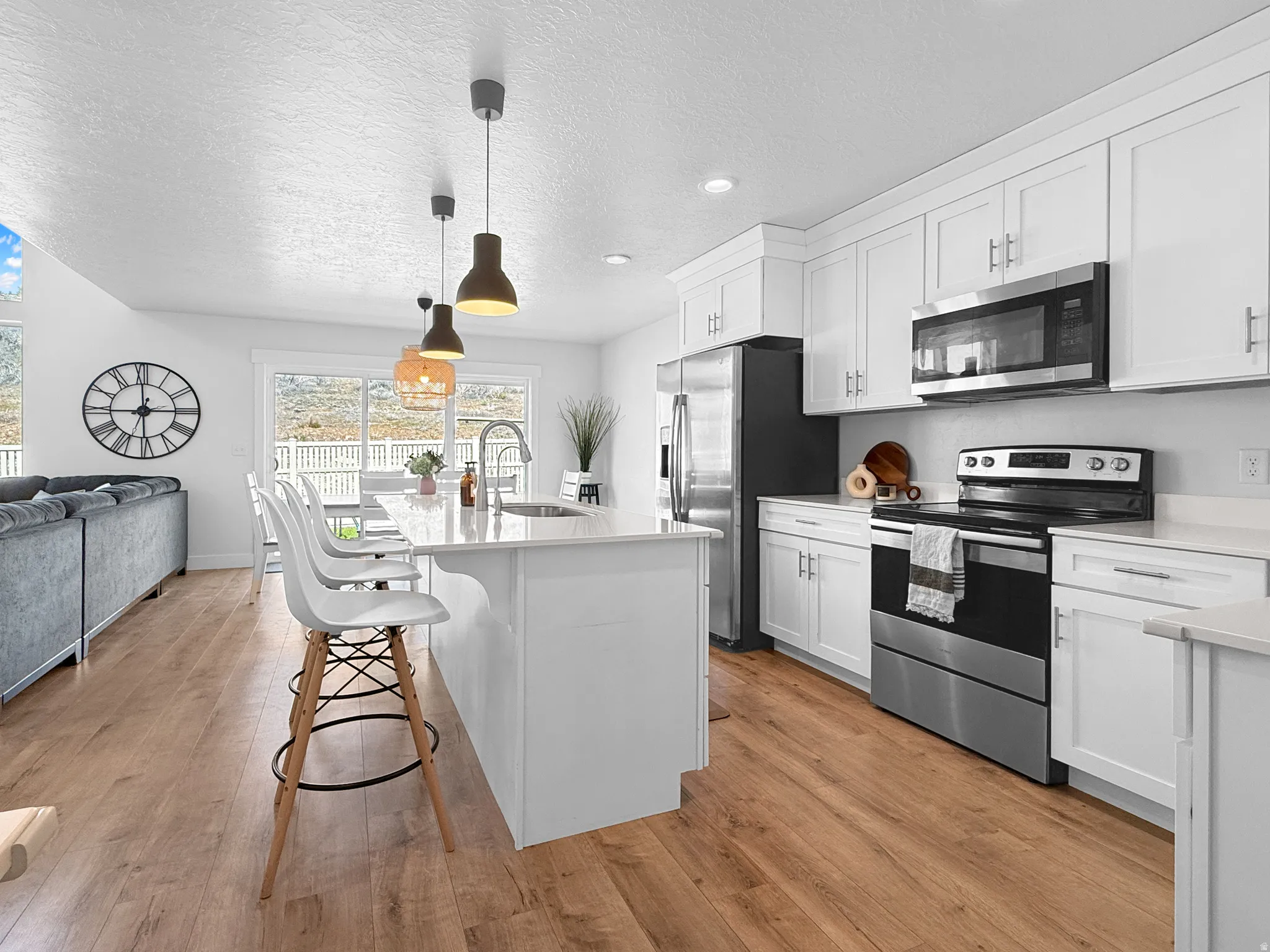 Bright kitchen featuring an island with seating, stainless steel appliances, white cabinetry, and wood-finish flooring