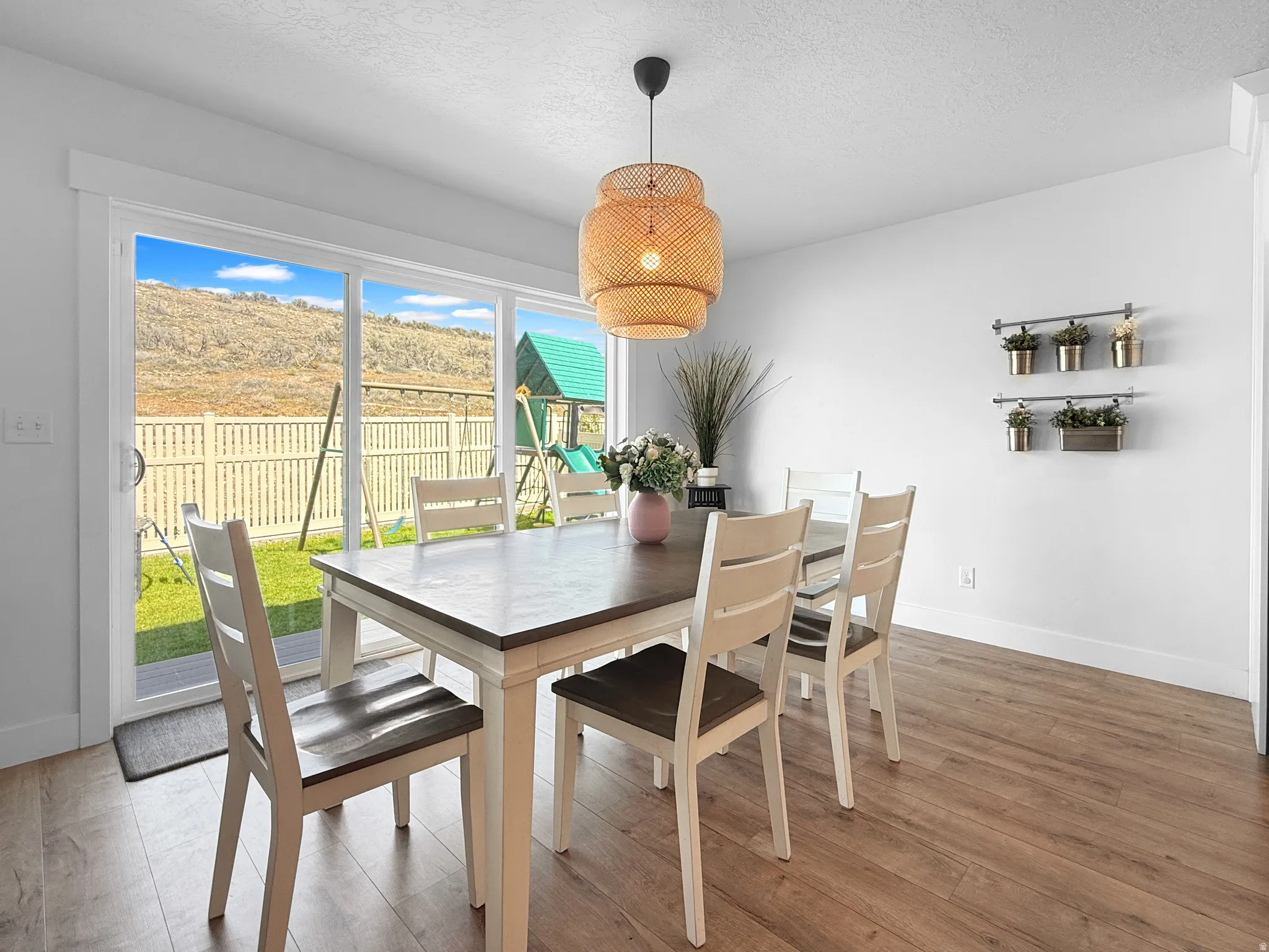 Spacious dining area featuring wood-finish flooring, a contemporary woven pendant light fixture, and a large sliding glass door opening to the exterior