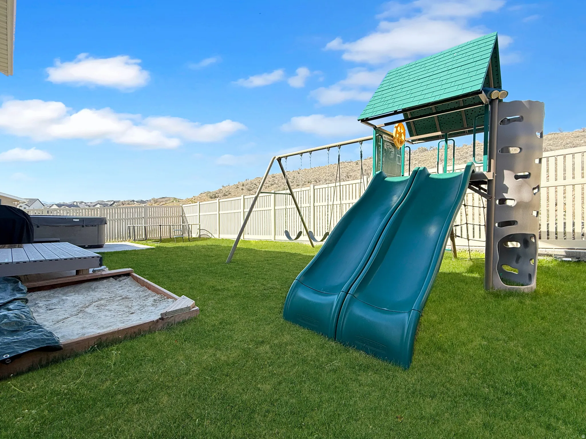Expansive backyard featuring a lush lawn, privacy fencing, and a built-in sandbox