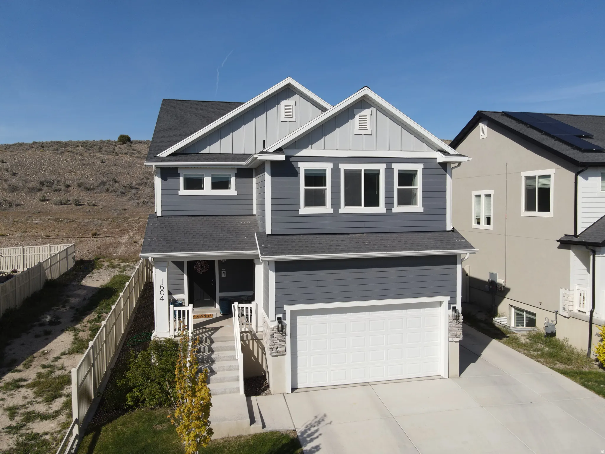 Two-story residential exterior featuring dark gray siding with white trim, a two-car garage, and a covered porch entry