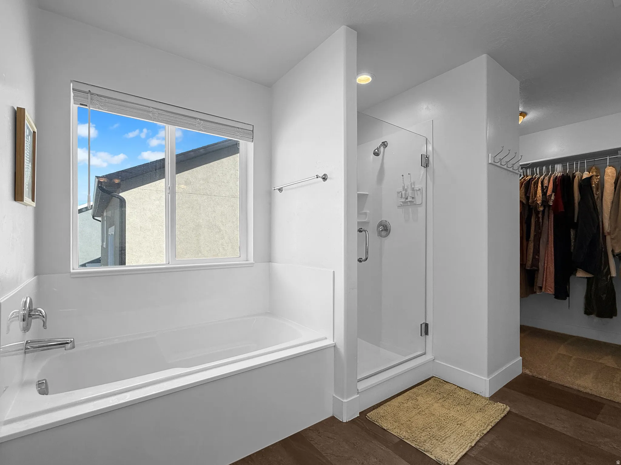 Bathroom featuring a built-in soaking tub with a window, a glass-enclosed shower, wood-finish flooring, and recessed lighting