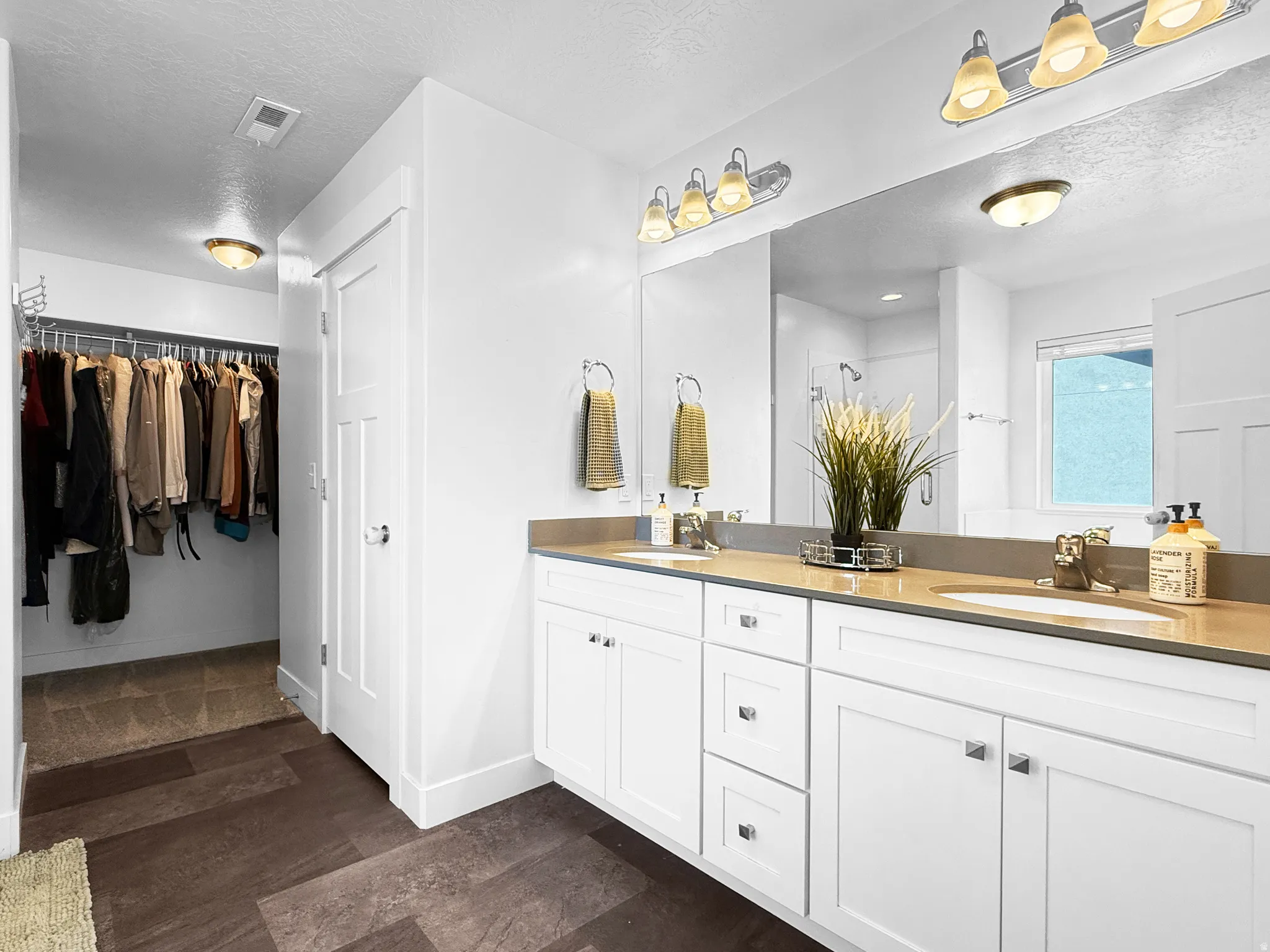 Bathroom featuring a double vanity with white cabinetry, light-toned countertops, and a full-width mirror