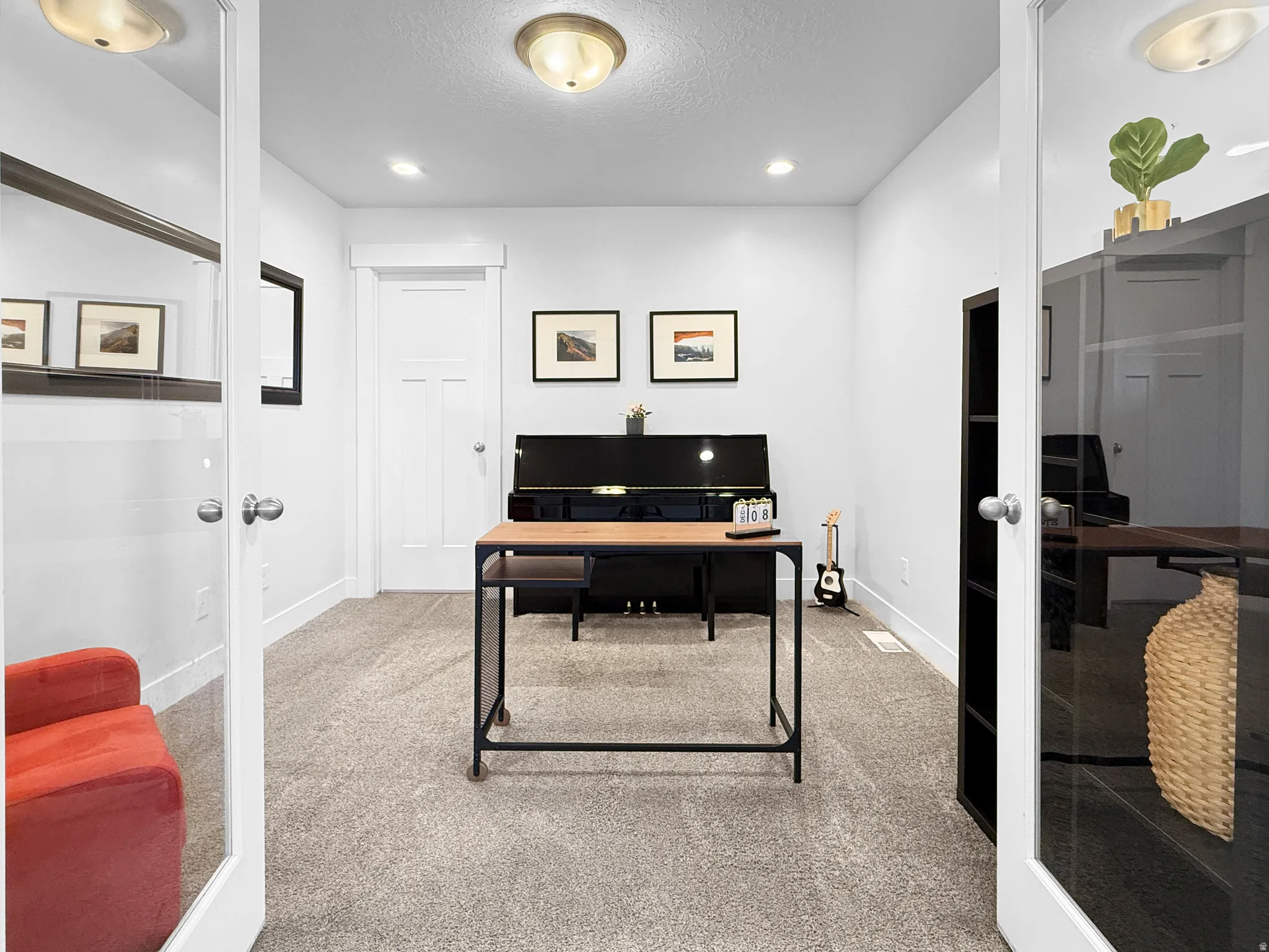 Double glass French doors opening into a versatile room with light-toned carpet flooring, recessed lighting, and a neutral wall color