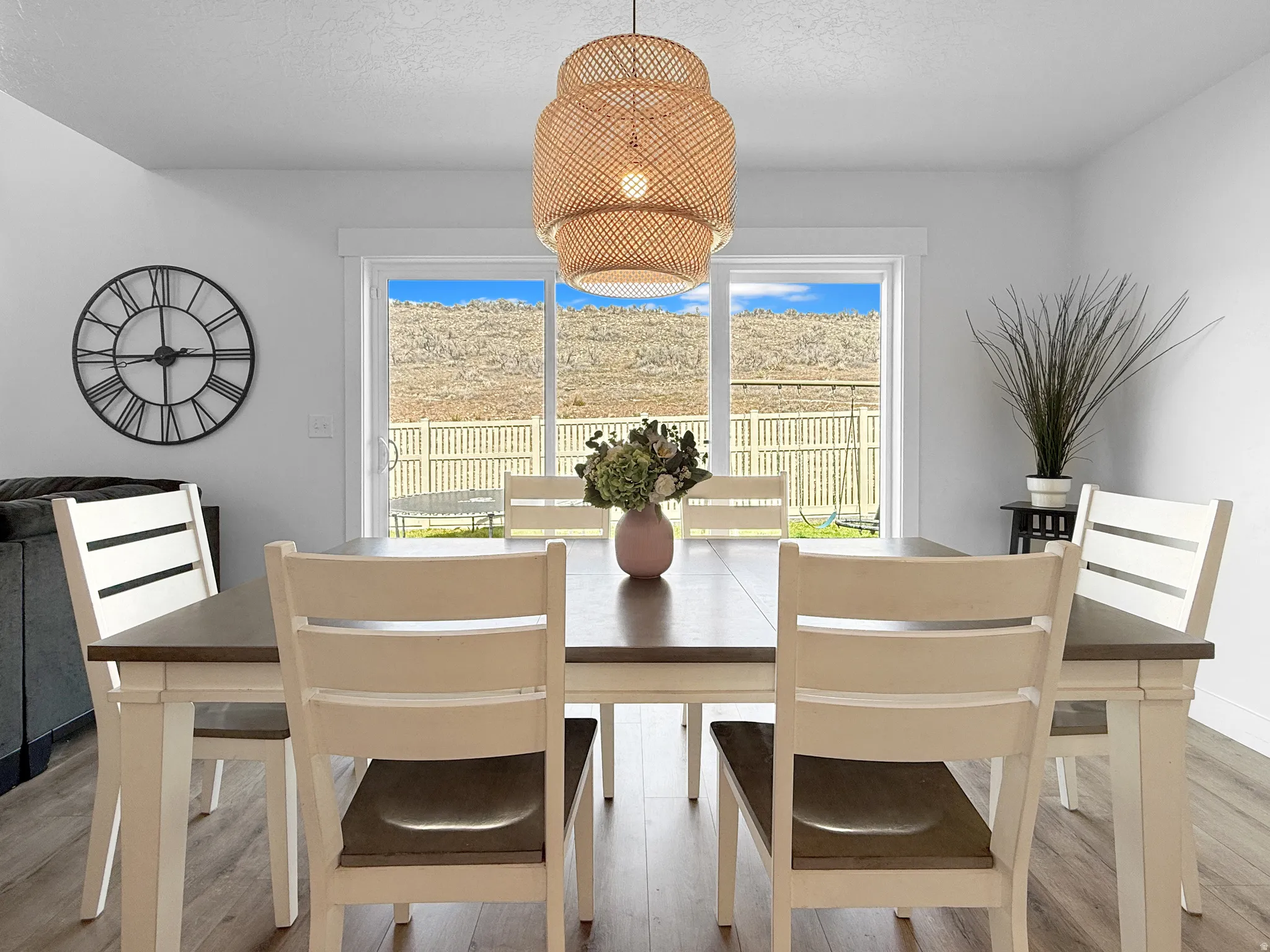 Dining area featuring a wood-finish table with white base, overhead rattan-style pendant light, and sliding glass door