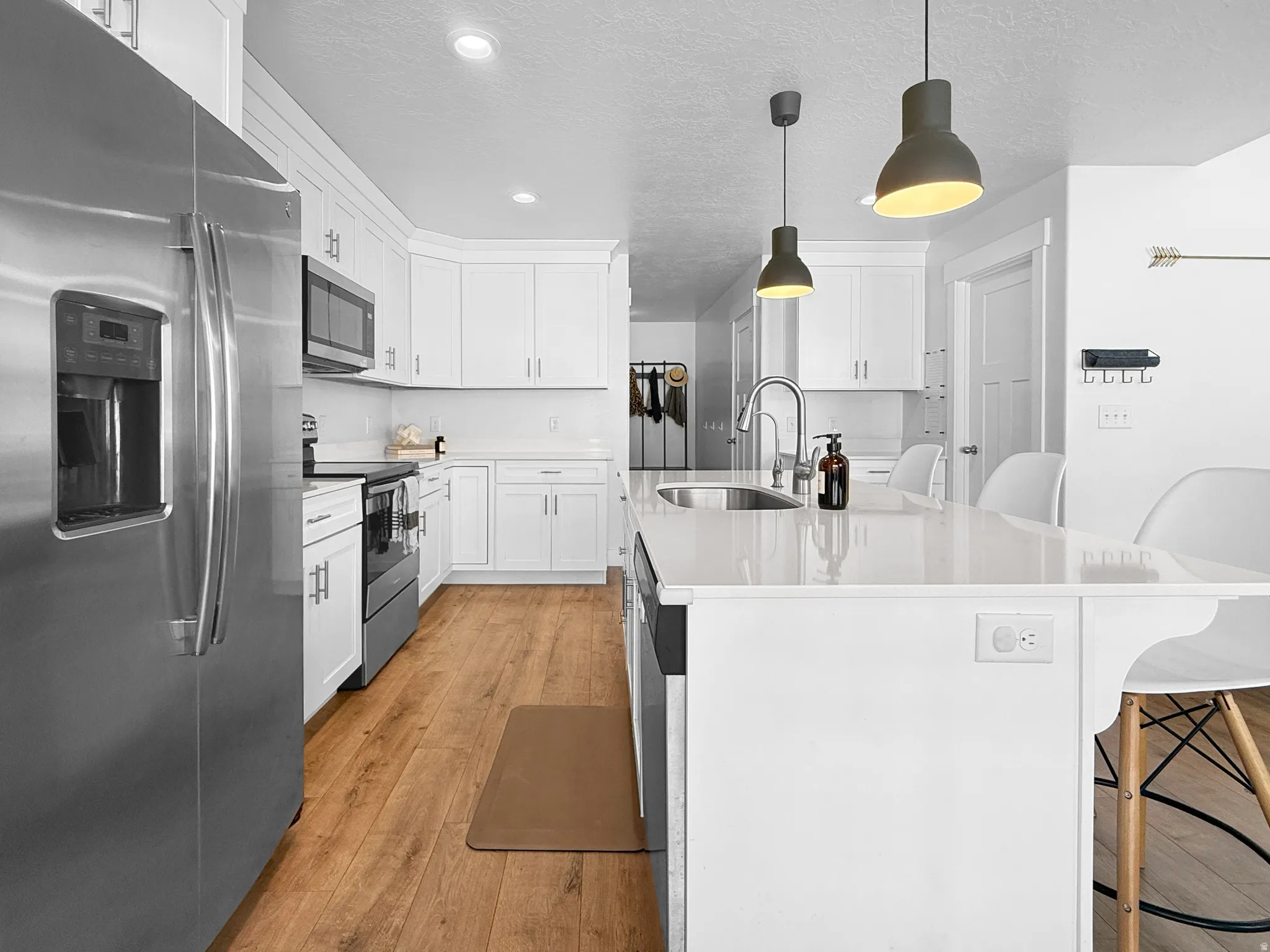 Contemporary kitchen featuring white cabinetry, stainless steel appliances, wood-finish flooring, recessed lighting, and a kitchen island with pendant lighting