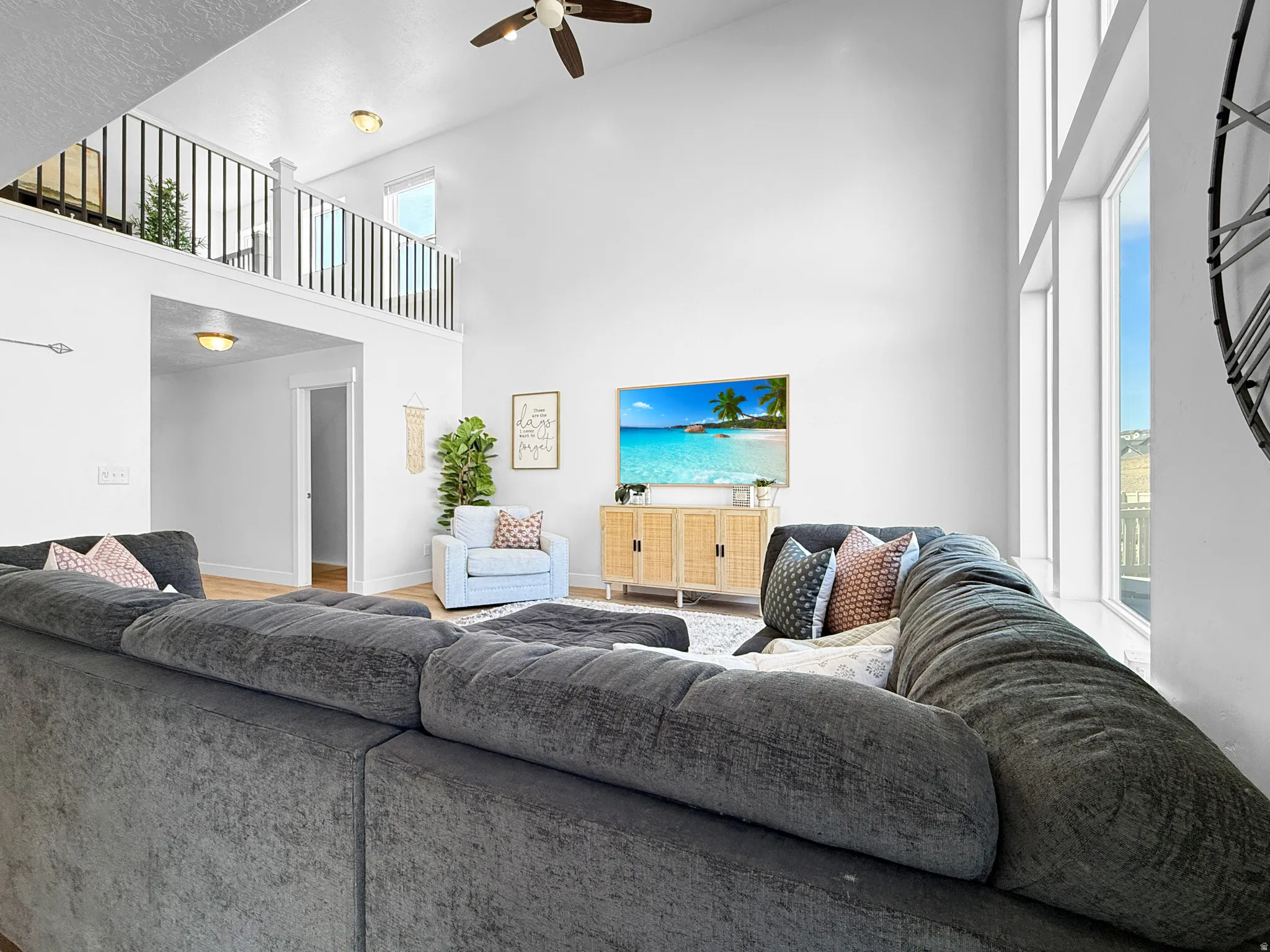 Spacious living area featuring a soaring vaulted ceiling, an upper-level balcony with black railing, and expansive windows