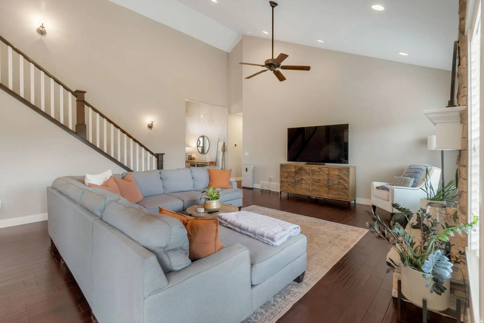Vaulted ceiling living area featuring dark wood-finish flooring, a contemporary ceiling fan, recessed lighting, and a staircase with white balusters and dark wood handrails