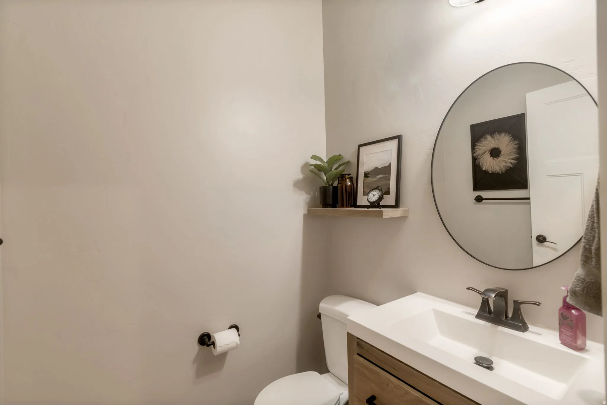 Modern powder room featuring a wood-finish vanity with an integrated sink, dark bronze faucet, and a large round mirror