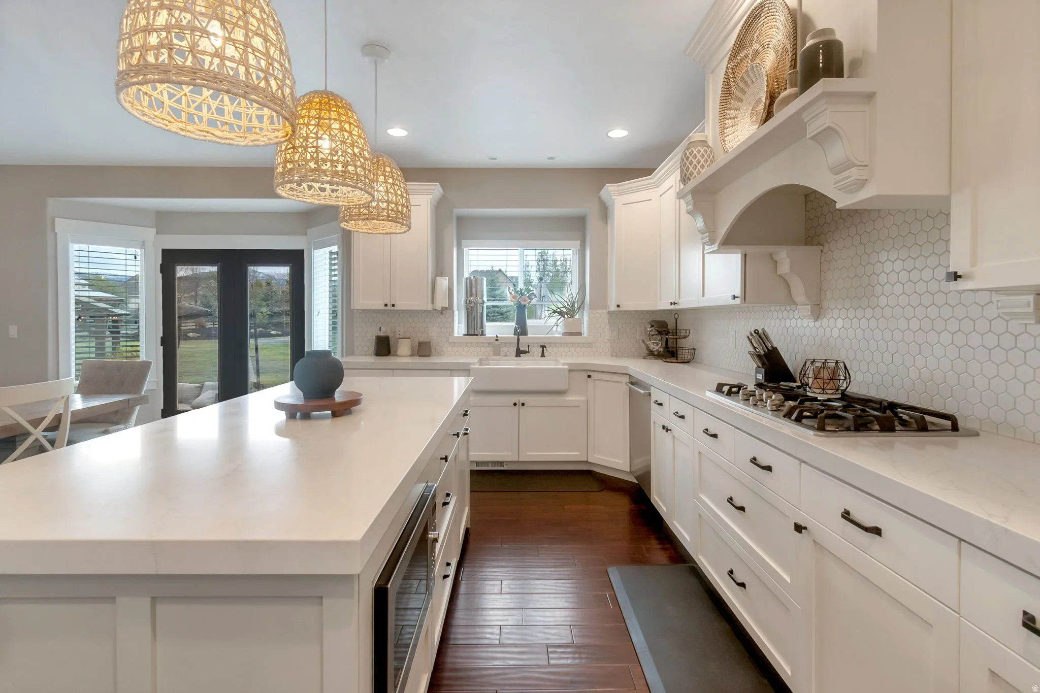 Contemporary kitchen featuring a large center island with integrated beverage cooler, rich wood-finish flooring, white cabinetry with dark hardware, a gas cooktop, and a hexagonal tile backsplash