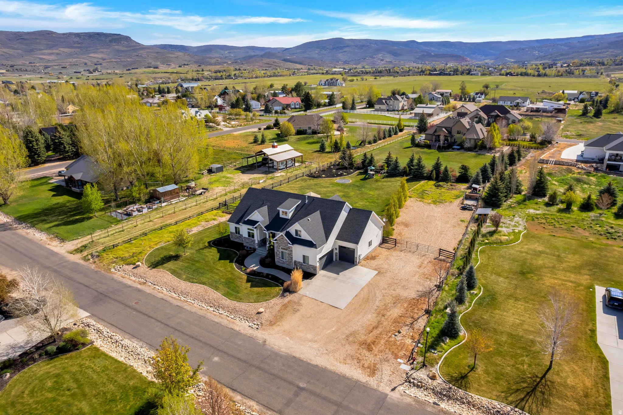 Contemporary residence featuring a light-colored exterior with stone accents, a dark shingle roof, and multiple gables