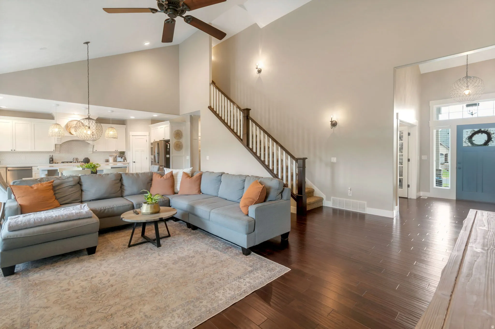 Expansive living space featuring wood-finish flooring, a vaulted ceiling with a ceiling fan, and a staircase with dark wood handrails and white balusters