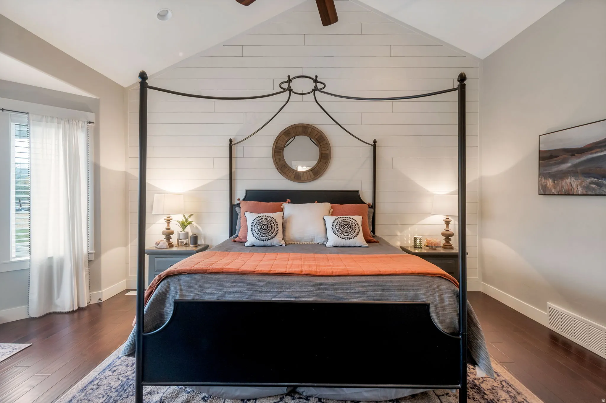 Bedroom featuring a vaulted ceiling with wood-finish flooring, a prominent shiplap accent wall, and a ceiling fan