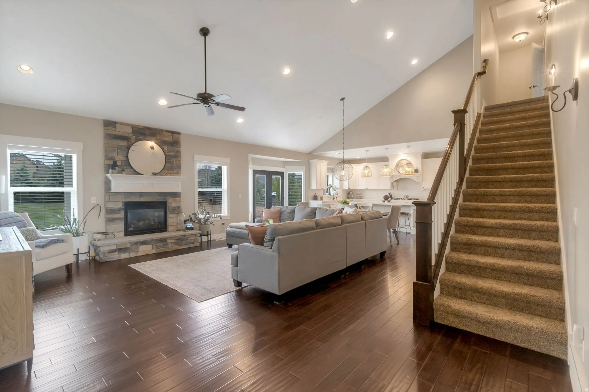 Vaulted ceiling great room featuring wood-finish flooring, a stone-surround fireplace with a white mantel, and recessed lighting