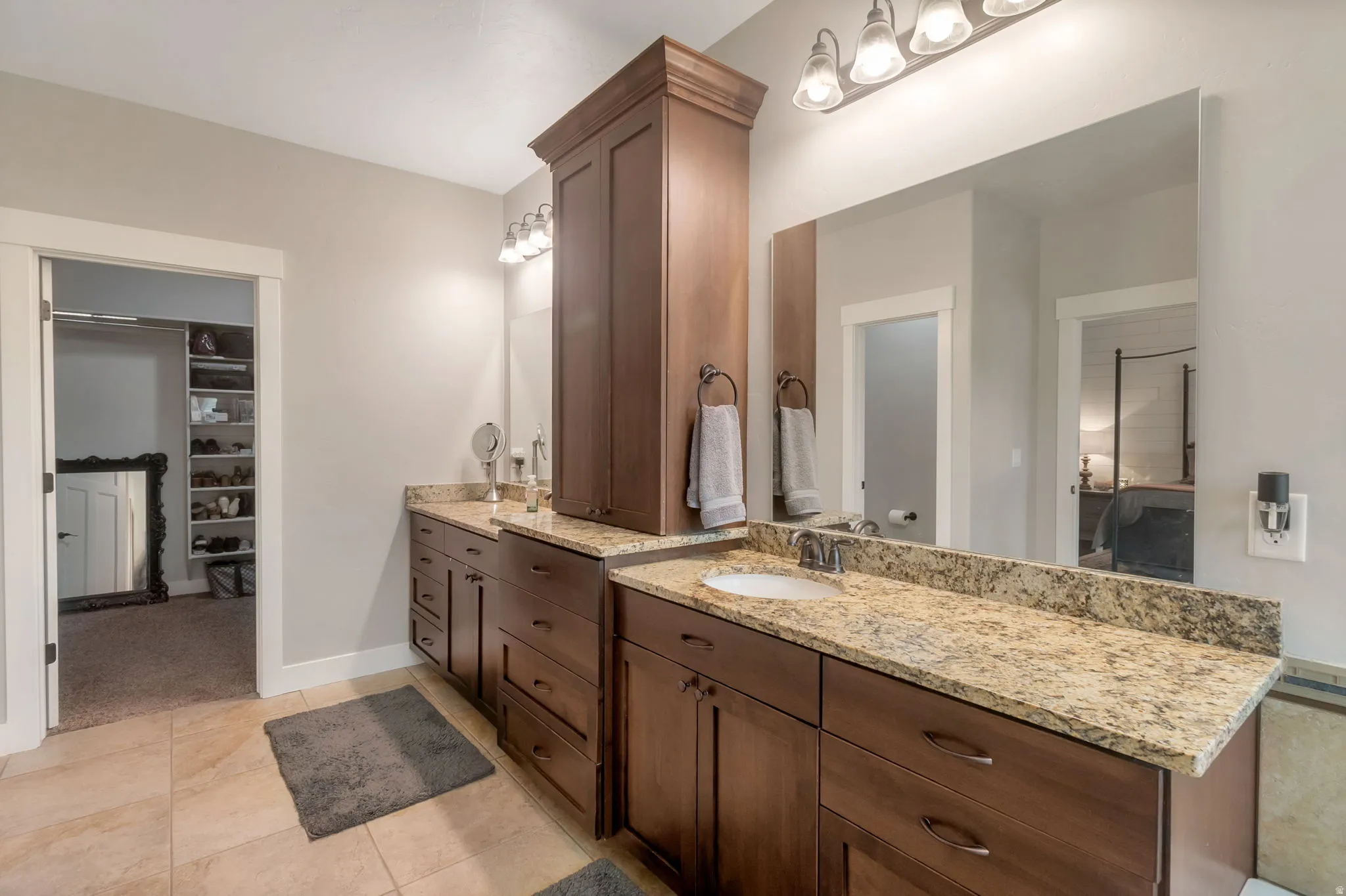 Bathroom featuring a dual vanity with granite countertops, rich wood cabinetry, and a full-width mirror