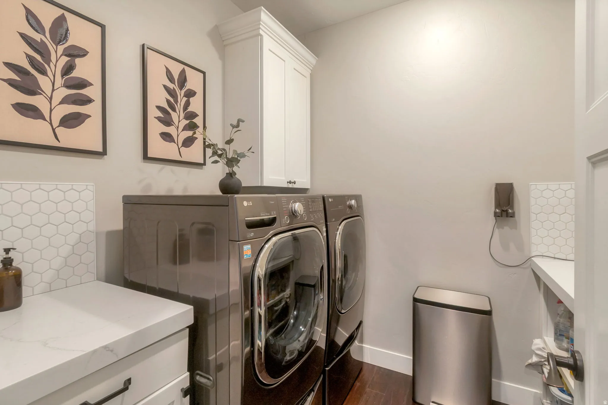 Laundry area featuring wood-finish flooring, white cabinetry, hexagon tile backsplash, and a white countertop