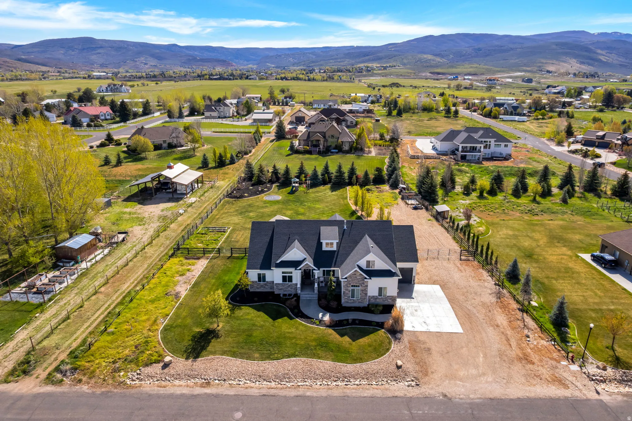 Expansive property featuring a modern residence with a dark roof and light-colored siding, a paved driveway, mature landscaping, and a fenced perimeter