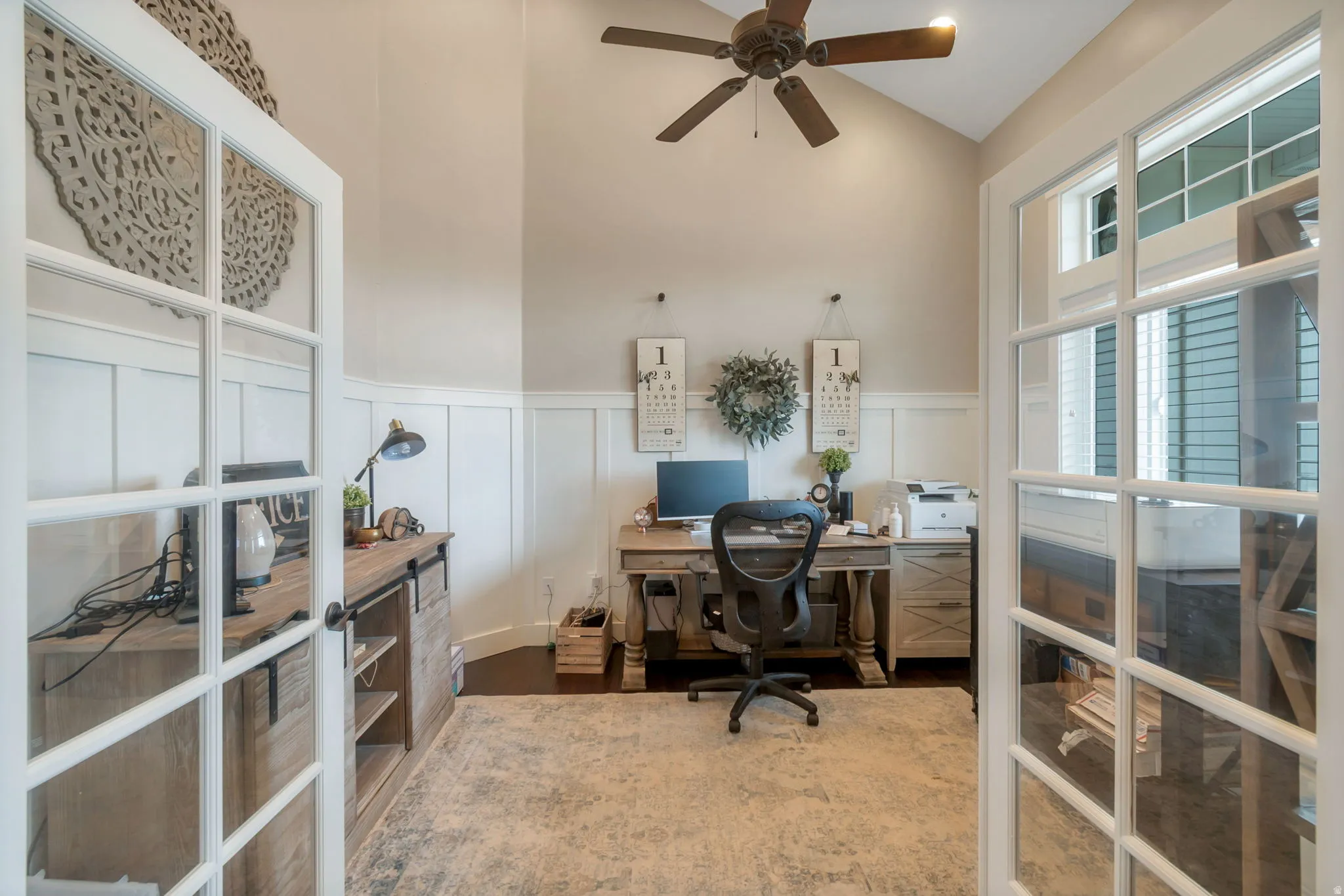 French doors opening into a dedicated room with a high vaulted ceiling, wood-finish flooring, a ceiling fan, and board and batten wainscoting