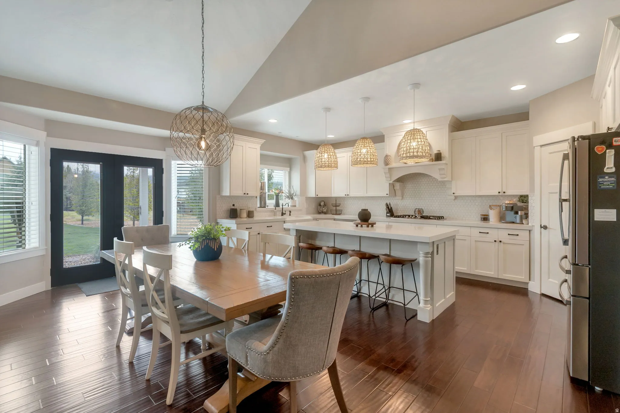 Open-concept kitchen and dining area featuring dark wood-finish flooring, white cabinetry, a central island with bar seating, and a white subway tile backsplash